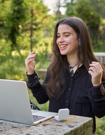 long-haired pretty woman with laptop doing video conference outdoors. teenager wearing headphones making a video call on a stone table outdoors with coffee. girl attending meeting by video call nature